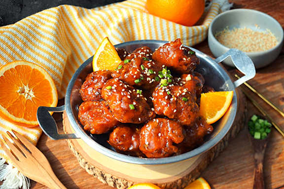 A bowl of glazed meatballs garnished with sesame seeds and green onions.