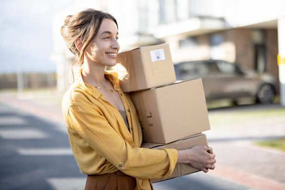 A woman is carrying a stack of cardboard boxes.