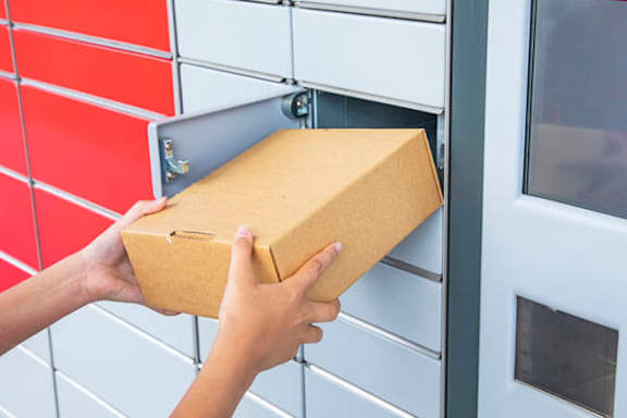 A person is putting a brown box into a grey mailbox.