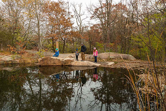 Three people standing on a rock over a pond.