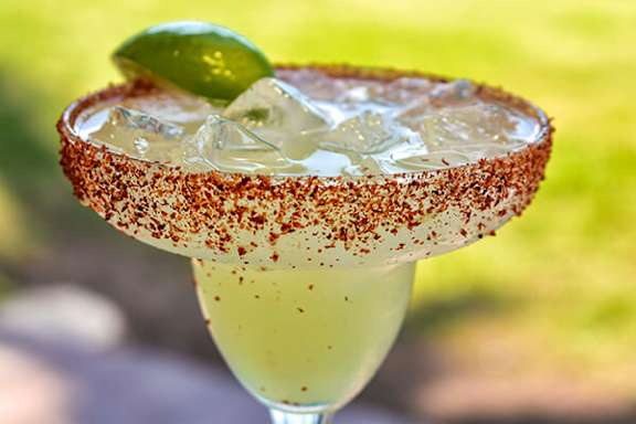 A margarita cocktail with a salted rim and a lime wedge on top.