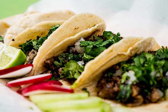 A close up of a taco with meat and vegetables.