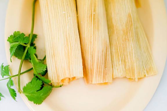 Plate of three tamales with a sprig of cilantro on the side.