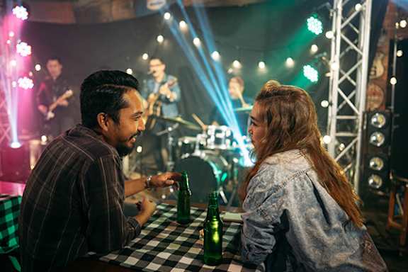 A man and a woman are sitting at a table in a dimly lit room with a band performing in the background.