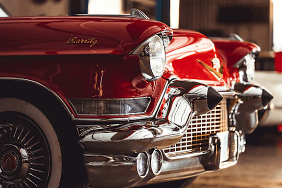 A red vintage car with a shiny chrome bumper.