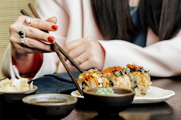 A woman is eating sushi with chopsticks.