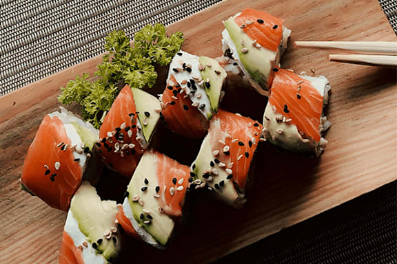 A wooden board with sushi rolls topped with sesame seeds and a green garnish.