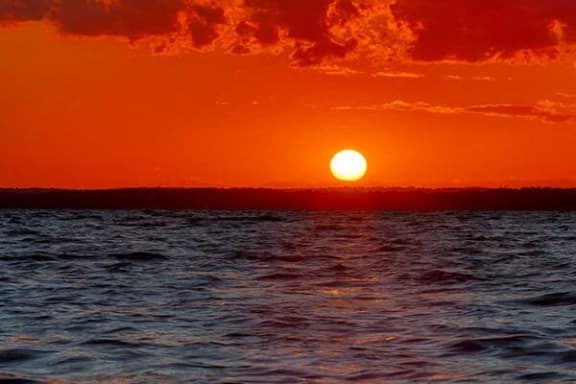 an orange sunset over the ocean with the sun setting in the sky