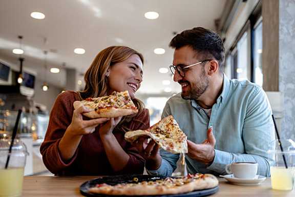 A man and a woman are sharing pizza in a restaurant.