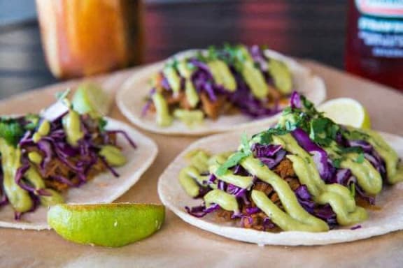 three tacos with vegetables and a lime on a table