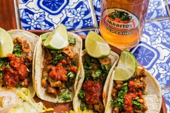 three tacos on a plate next to a glass of beer