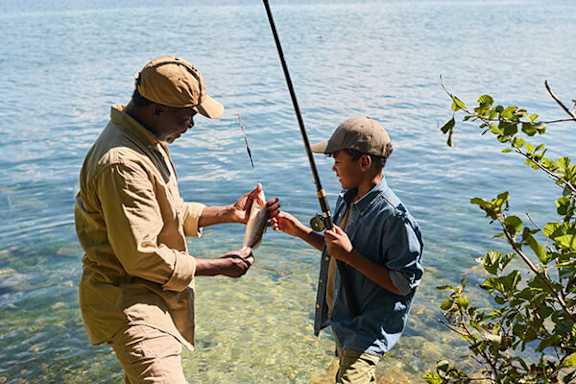 A man in a yellow shirt and a boy in a blue shirt are fishing in the water.