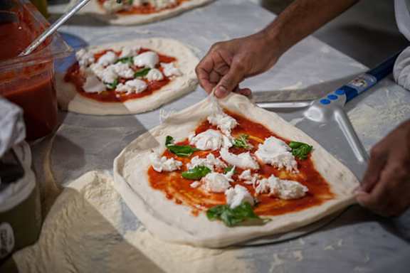 A person is making a pizza with tomato sauce and cheese.