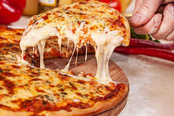 A person is pulling a slice of cheese pizza from a whole pizza.