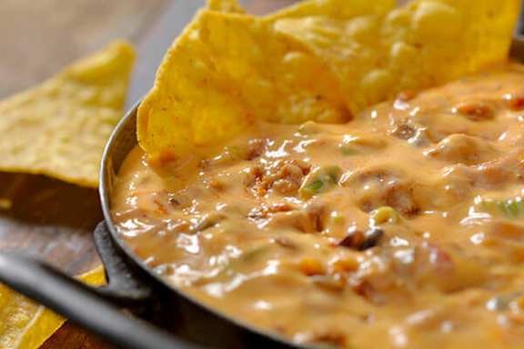 A skillet of cheesy dip with tortilla chips on the side.
