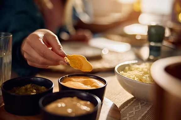 A person dips a potato chip into a bowl of cheese dip.