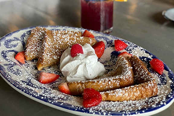 A plate of french toast with strawberries and whipped cream.