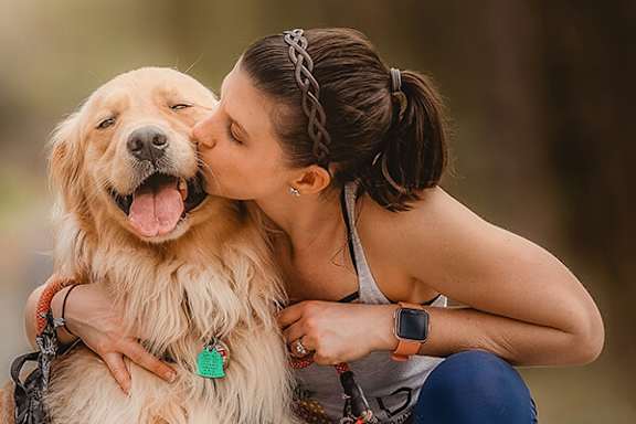 A woman is kissing a golden retriever on the cheek.