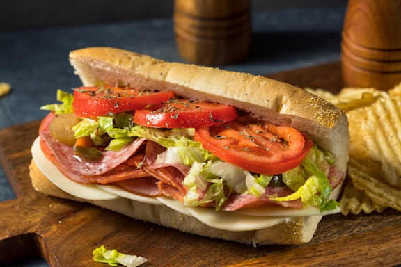 A sandwich with ham, cheese, lettuce, and tomato slices on a wooden board.