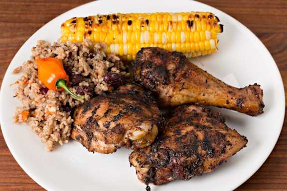 A plate of food with grilled chicken, corn on the cob, and a side of rice and beans.