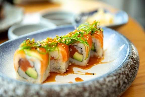 A plate of sushi with a piece cut in half, topped with sauce and garnish.
