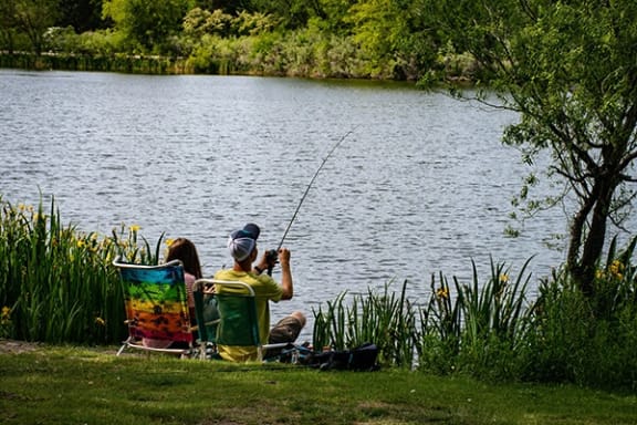two people sitting by a lake with fishing rods