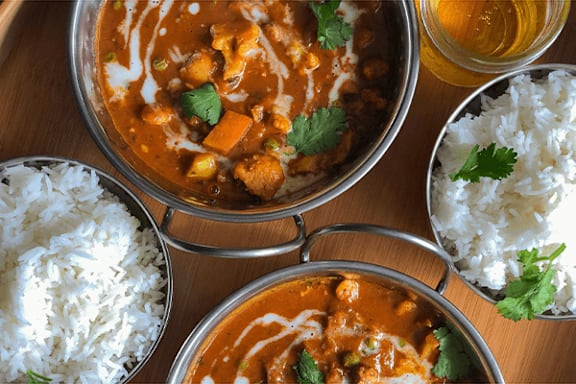 A bowl of curry with rice and a glass of beer on the side.