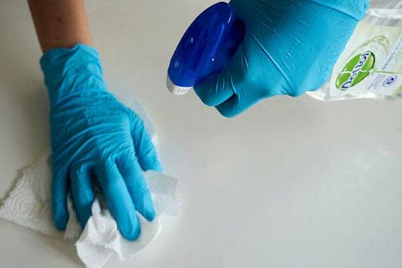 A person wearing blue gloves is cleaning a surface with a white cloth.