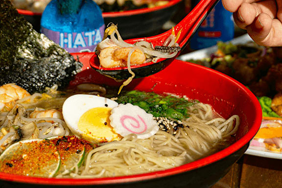 A bowl of noodles with a boiled egg, seaweed, and other toppings is being served with chopsticks.