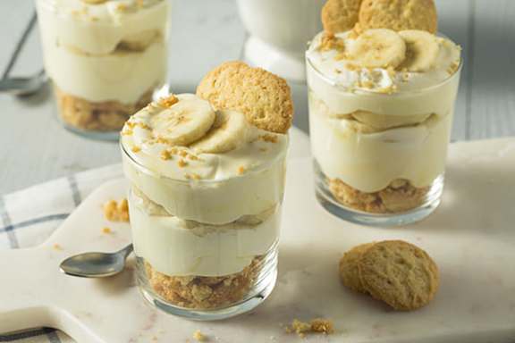 A dessert in a glass with banana slices and cookies on top.