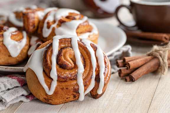 A cinnamon roll with white icing on top is placed on a plate.