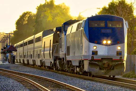 A blue and silver train is on the tracks with trees in the background.