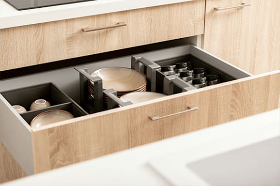 A drawer in a wooden cabinet is open, revealing a plate, a bowl, and some jars.