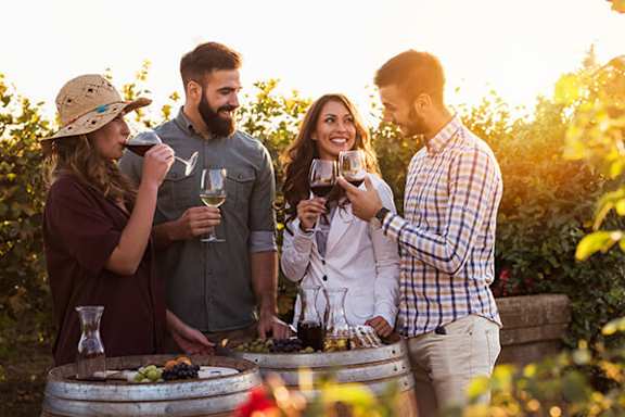 Four people standing around a barrel of wine.