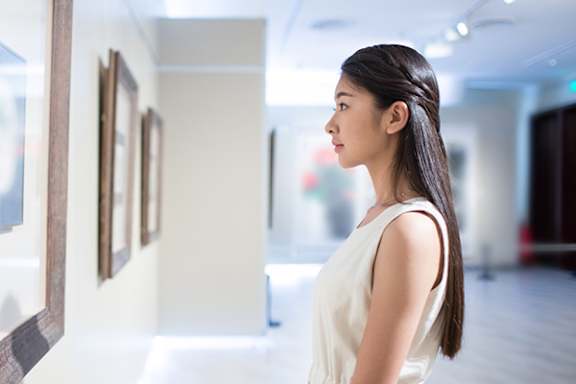Three people are walking past paintings in a museum.