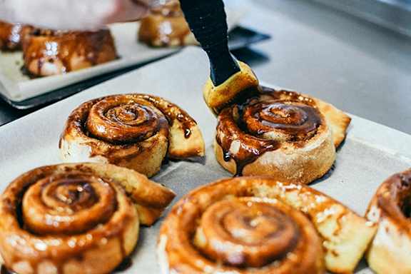 A person is spreading a topping on cinnamon rolls.