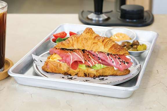 A sandwich with ham, salmon, and avocado on a croissant.