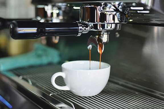 A white cup is being filled with coffee from a silver espresso machine.