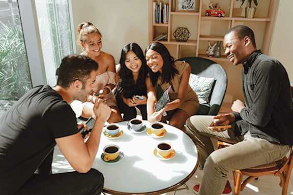 A group of people are sitting around a table with cups and saucers on it.