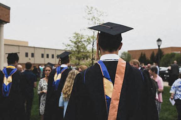 A group of people in graduation gowns and caps are walking in a line.
