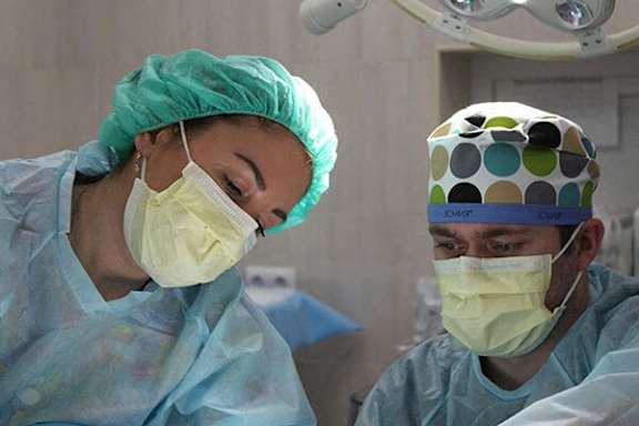 Two surgeons wearing surgical masks and caps are in an operating room.