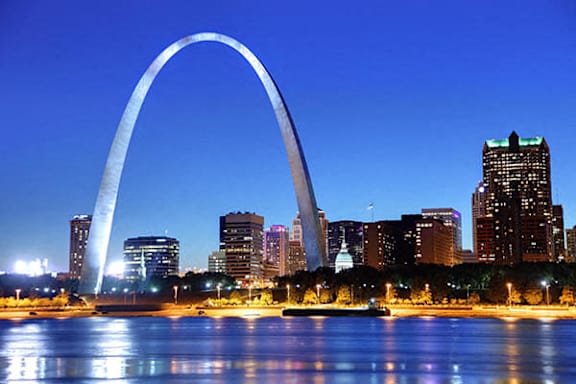 The image features a large arch structure in the foreground with a city skyline in the background.