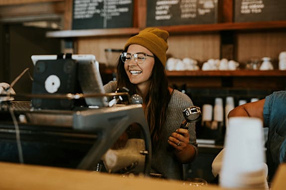 A woman in a yellow beanie is smiling while working at a coffee shop.