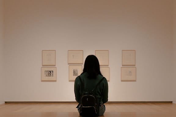 A woman sits in a gallery looking at artwork.