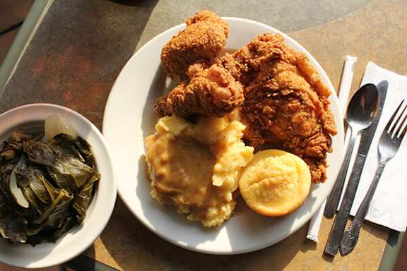 A plate of fried chicken, biscuits, and gravy with a side of collard greens.