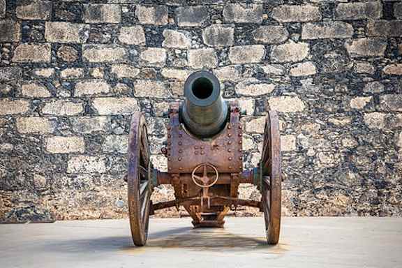 An old cannon is on display in front of a stone wall.