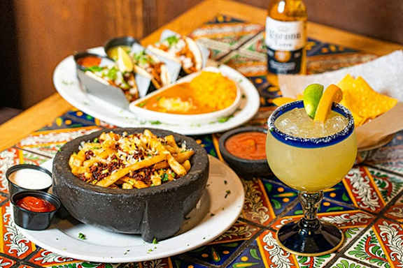 A bowl of nachos and a margarita glass on a colorful table.