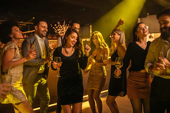 A group of people dancing and holding wine glasses at a party.