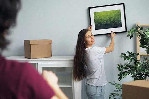 A woman is hanging a picture on a wall.