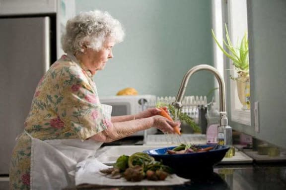 an older woman in the kitchen washing vegetables in the sink